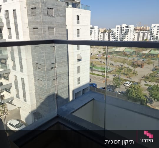 מעקה זכוכית שקוף מותקן במרפסת עם מאחז יד כהה ונוף עירוני